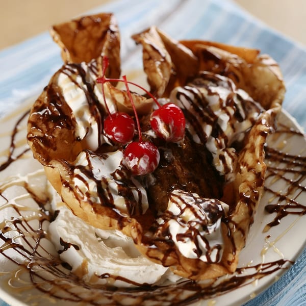 Fried ice cream dessert in a crispy shell, topped with whipped cream, chocolate, and cherries.