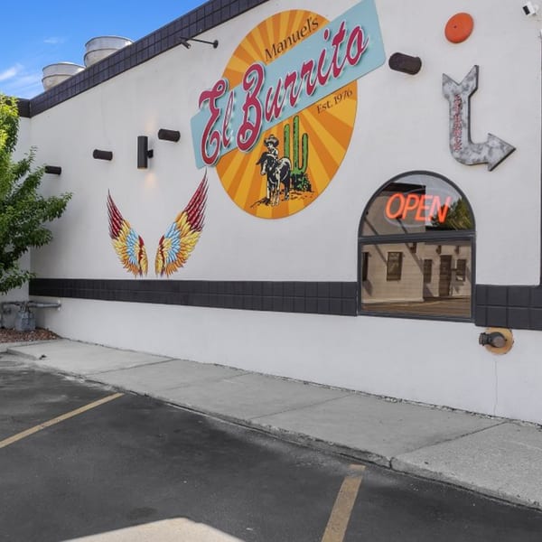 Exterior of Manuel's El Burrito Restaurant, featuring a large sign, colorful wings mural, and an "OPEN" sign.