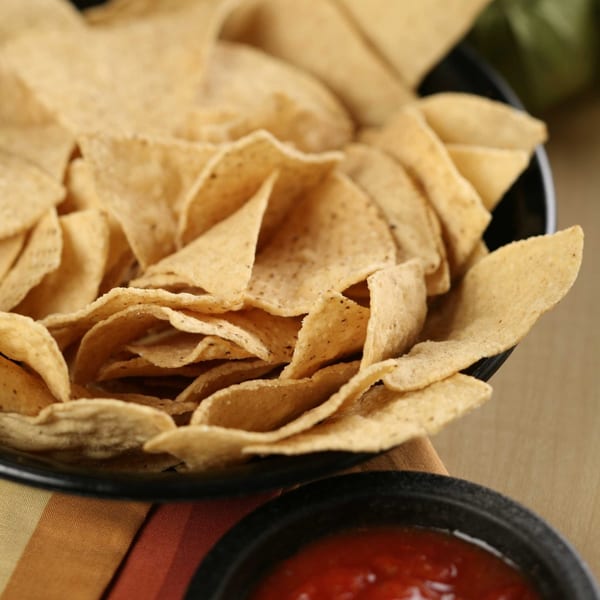A black bowl overflowing with crispy tortilla chips, with a small bowl of salsa in the foreground.