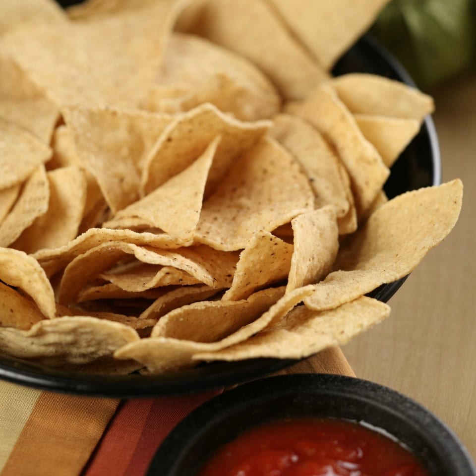 A black bowl overflowing with crispy tortilla chips, with a small bowl of salsa in the foreground.