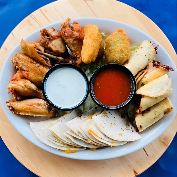 A platter of Mexican appetizers including chicken wings, jalapeño poppers, taquitos, and quesadillas with dipping sauces.