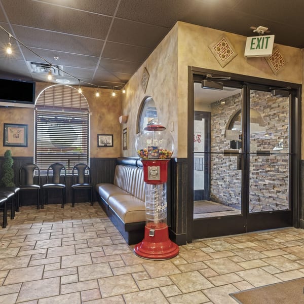 Waiting area with a red gumball machine, booth seating, black chairs, and an exit sign.